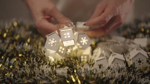 Hands turning on battery-powered string lights shaped like small white houses Stock Footage 323348588