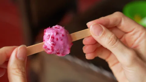 Hands Turning a Berry Popsicle with Fruit Pieces Before Taking a Bite Видео 290908413