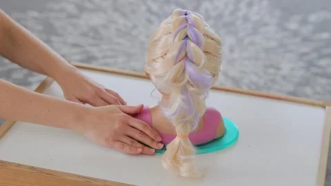 Hands turning child mannequin head with blonde dragon braid hairstyle Stock Footage 331997402