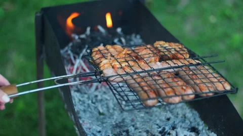 Hands turning grid with roasted chicken thighs. Grilling sausages meat on Stock Footage 251738306