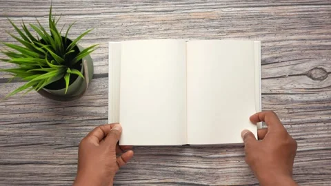 Hands turning pages of blank notebook on wooden table with potted plant. Stock Footage 333153808