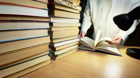 Hands turning pages of book on desk in library near lamp, Stock Footage 220176395
