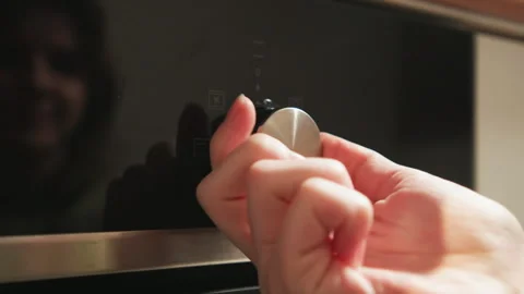 Hands turning stainless steel control knob on glossy black oven panel with Stock-Footage 345675371