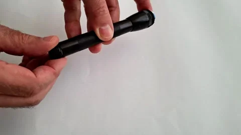 Hands Twist Tail Cap of Black LED Flashlight Stock Footage 332890599