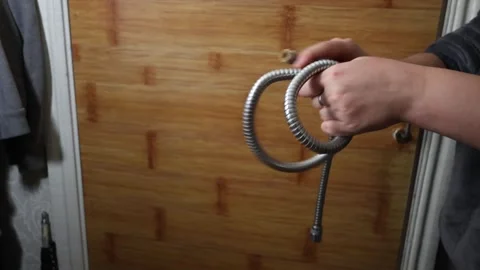 Hands twisting a flexible metal shower hose into a knot against a wooden Stock Footage 339181005