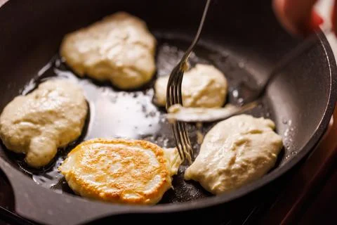 Hands with two forks flipping semi-liquid dough roasting on cast iron pan Photos