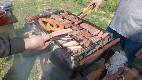 Hands of two men checking and turning meat on a barbecue Stock Footage 274430662