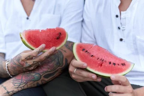 Hands of two men holding a piece of watermelon sitting together on the beach Stock Photos