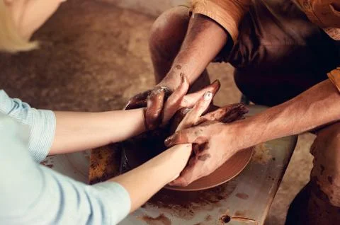 Hands of two people create pot on potter's wheel. Teaching pottery, carftman's Stock Photos