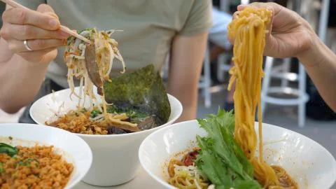 Hands of two people pulling noodles out of ramen soups. Healthy trendy Asian Stock Photos
