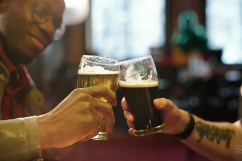 Hands of two young intercultural men clinking with glasses of beer in the pub Stock Photos