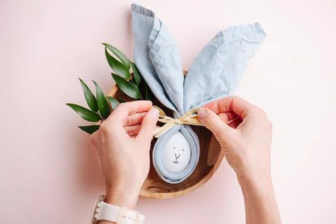 Hands tying a bow-knot on an easter egg in a napkin. Top view. Stock Photos