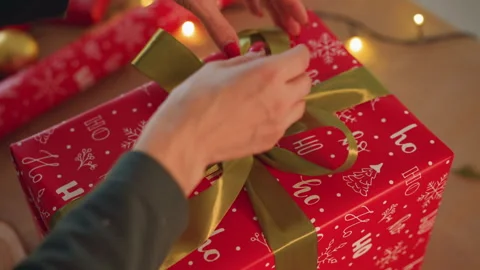 Hands tying green ribbon on present, warm fairy lights, gold baubles, red Stock Footage 333305921