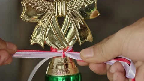 Hands tying a red and white satin ribbon onto the neck of a golden trophy w.. Video stock 324823238