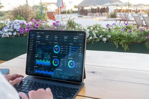 Hands type on a keyboard attached to a tablet displaying financial charts and Stock Photos