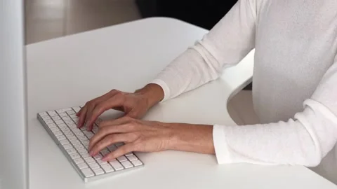 Hands typing on bright white keyboard, beige sleeve blending into modern desk Stock-Footage 288244992
