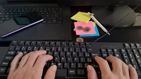 Hands typing on a computer keyboard with a smartphone and sticky notes nearby Stock Footage 340241301