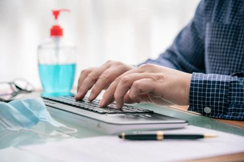 Hands typing computer while teleworking with mask and hydrogel on the table Foto stock