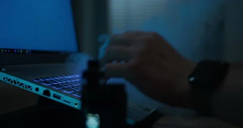 Hands typing on a keyboard in a dark room, smoking a vape exhaling smoke nervous Stock Footage 239286990