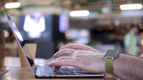 Hands typing on laptop, blurred cafe background, focused work vibe Stock Footage 342077611