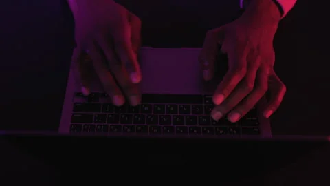 Hands typing on laptop keyboard in dark room with neon red and purple light Stock Footage 326071839