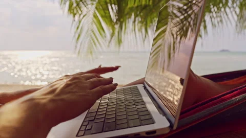 Hands Typing on Laptop Keyboard in Hammock With Palm Leaves Reflection and Brigh Stock Footage 326969411