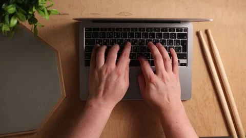 Hands typing on a laptop keyboard next to drumsticks on a wooden desk Vidéo 341737547