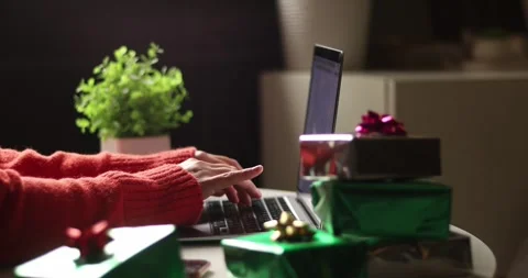 Hands typing on laptop surrounded by Christmas gifts and a small plant Stock Footage 339072981