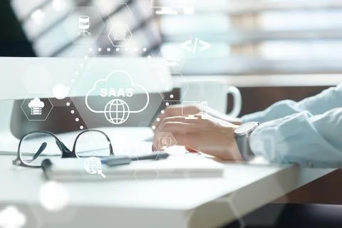 Hands typing on a laptop at a workspace with Saas graphics in the background Stock Photos