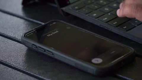 Hands typing on portable computer next to active smartphone call from "My Dad", Stock Footage 340485868