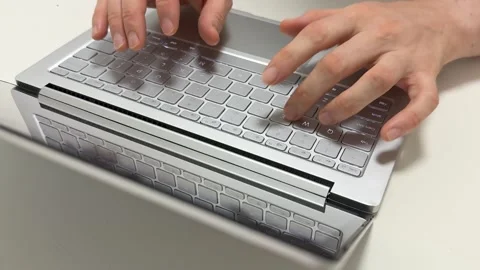 Hands typing quickly on a light gray laptop keyboard in the morning for work or Video stock 316456508