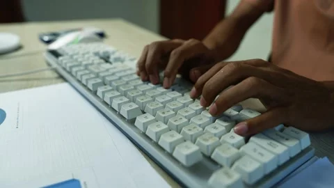 Hands typing on a white computer keyboard beside printed charts and office .. Stock Footage 345119074