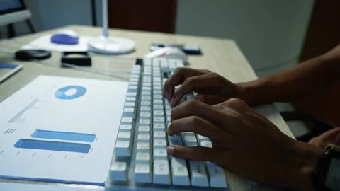 Hands typing on a white computer keyboard beside printed business charts on.. Stock Footage 345119085
