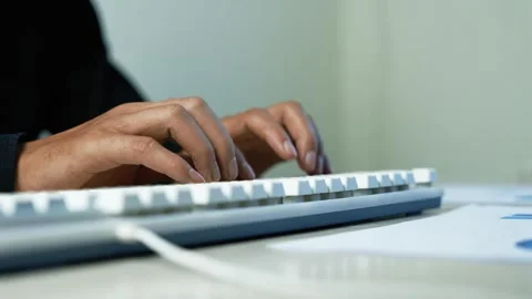 Hands typing on a white computer keyboard at a desk, with papers nearby in .. Stock Footage 345119105