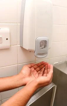 Hands under an automatic wall mounted soap dispenser. Stock Photos