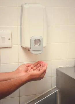 Hands under an automatic wall mounted soap dispenser. Stock Photos
