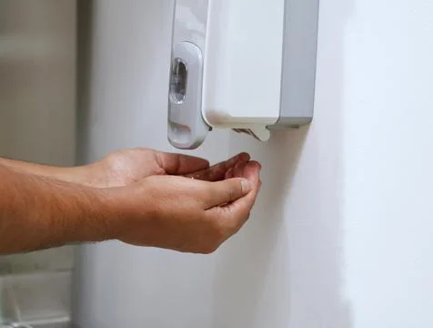 Hands under an automatic wall mounted sanitizer dispenser. Stock Photos