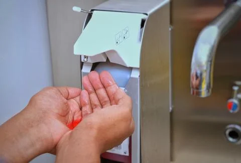 Hands under an automatic wall mounted soap dispenser. Stock Photos