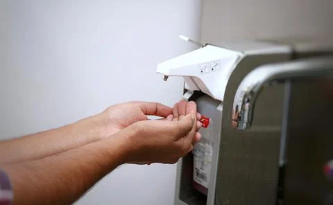 Hands under an automatic wall mounted soap dispenser. Stock Photos