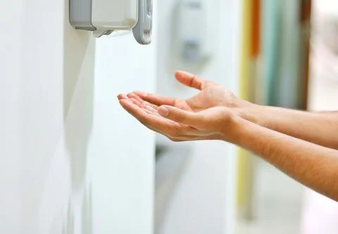 Hands under an automatic wall mounted sanitizer dispenser Stock Photos