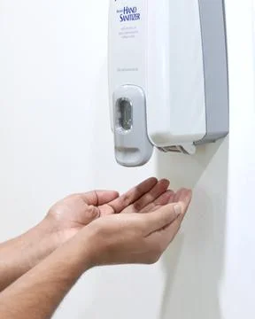 Hands under an automatic wall mounted sanitizer dispenser. Stock Photos