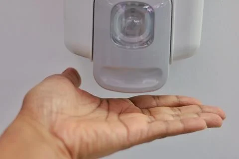 Hands under an automatic wall mounted sanitizer dispenser. Stock Photos