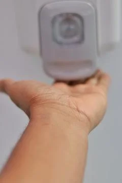Hands under an automatic wall mounted sanitizer dispenser. Stock Photos