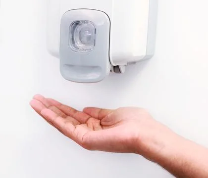 Hands under an automatic wall mounted sanitizer dispenser. Stock Photos