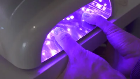 Hands under UV nail lamp during the gel manicure curing process Stock Footage 298300410