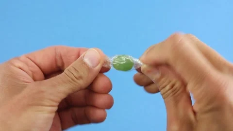 Hands unfold one green candy lollipop on blue background Video stock 156474682