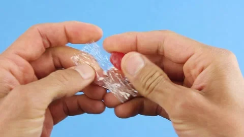 Hands unfold one red candy lollipop, unhealthy sugar sweets and plastic garbage Stockbeeldmateriaal 156474681