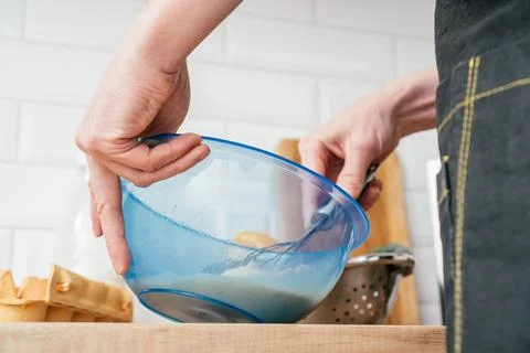 Hands of unrecognizable man in black kitchen apron beating eggs in blue plastic Stock Photos
