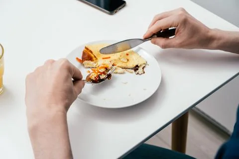 Hands of unrecognizable man cutting with table knife and eating omelette with Foto stock