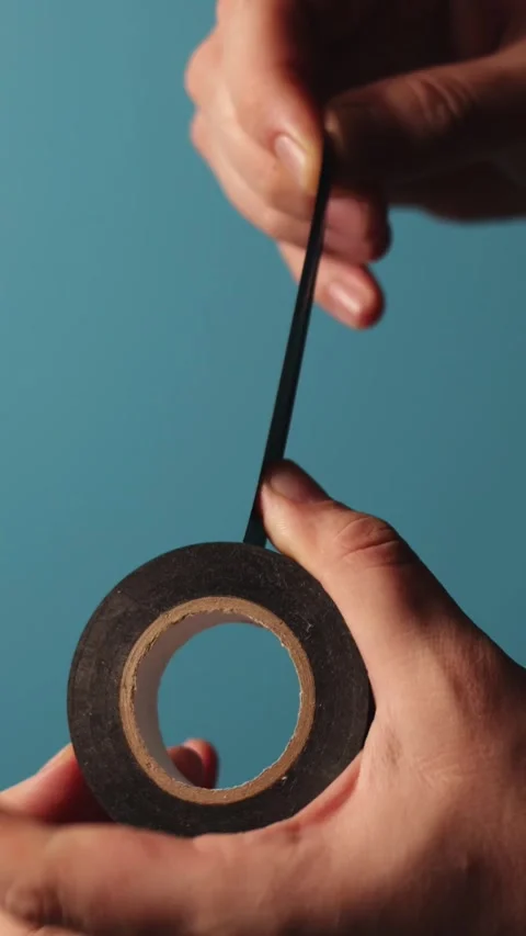Hands unrolling black electrical tape against a blue background Stock-Footage 343838053